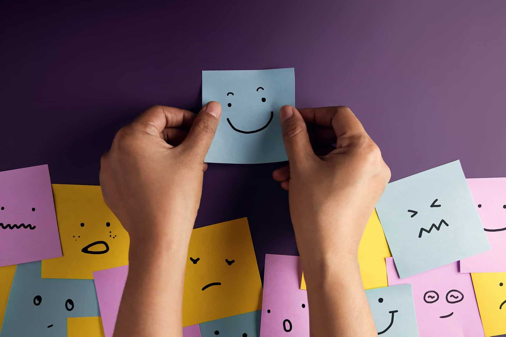 A person placing sticky notes on a table, each with a face drawn to show different feelings