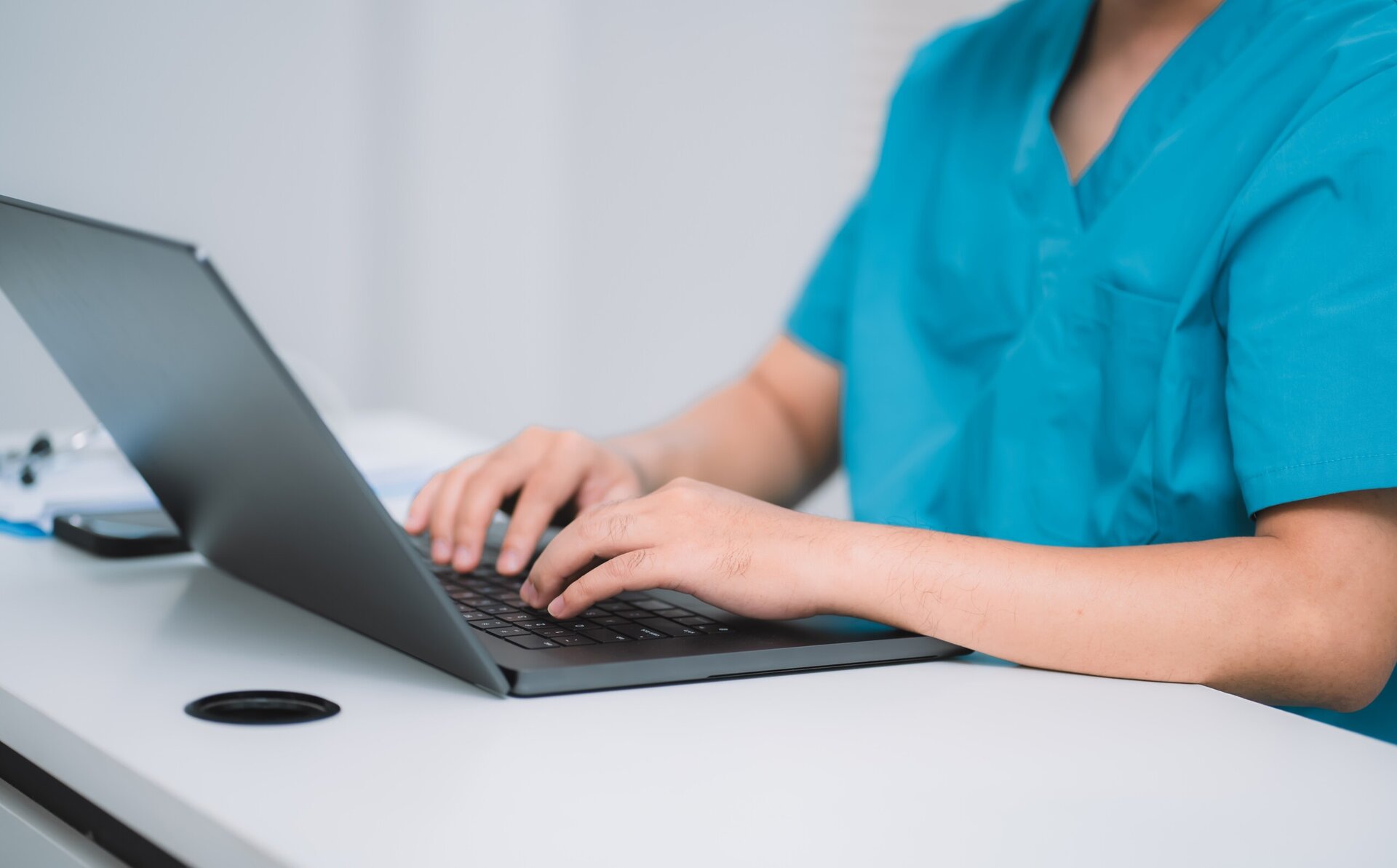 A Young Asian male doctor with glasses sitting at desk, looking at screen, working intently on laptop in office. Professional therapist writing report or email, Work stress